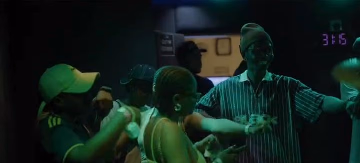 Dancers in caps and a striped shirt move together under green light