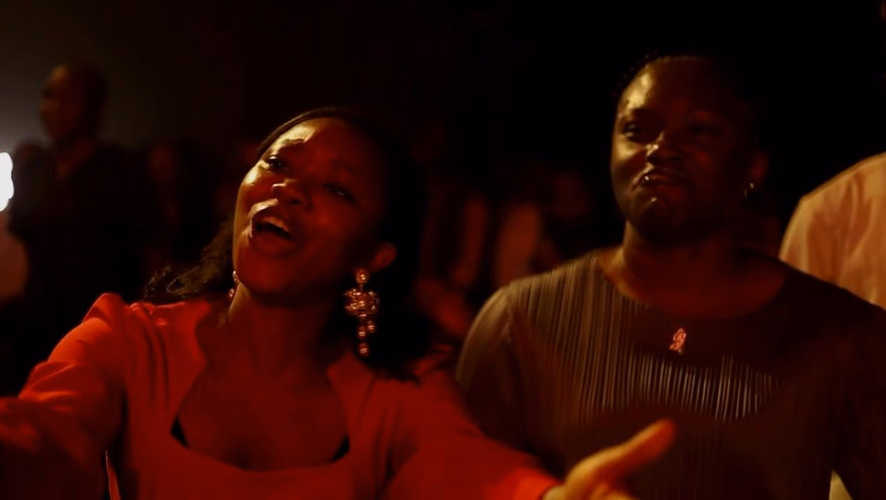 A woman in red sings with her eyes closed beside a smiling man in the congregation