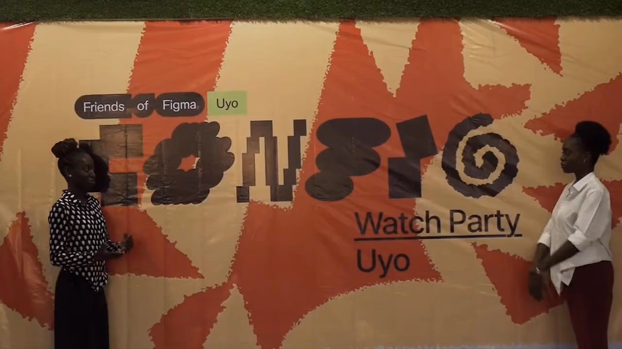 Two women stand in front of the orange Config Watch Party Uyo backdrop with the Friends of Figma sign