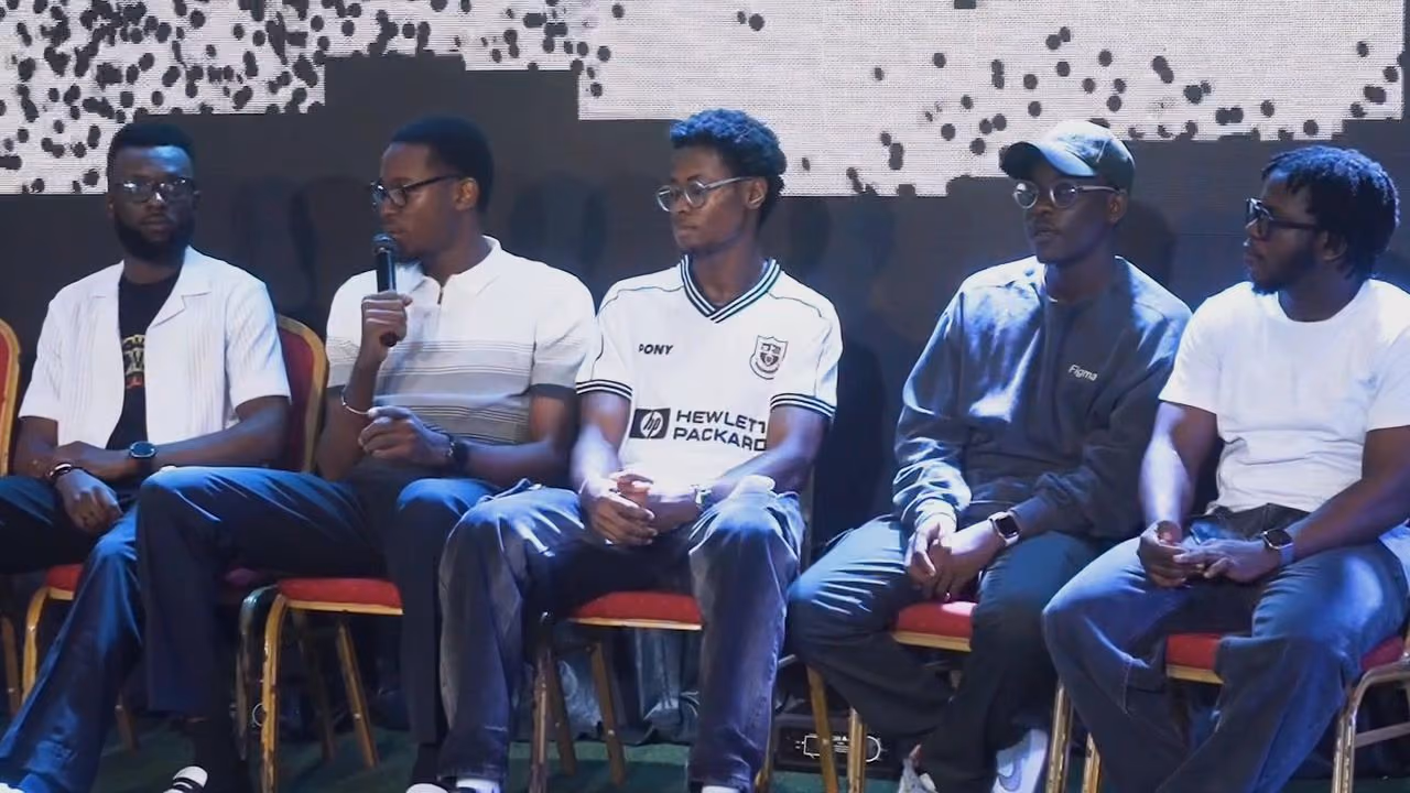 A panel of five designers seated on stage, one speaking into a microphone