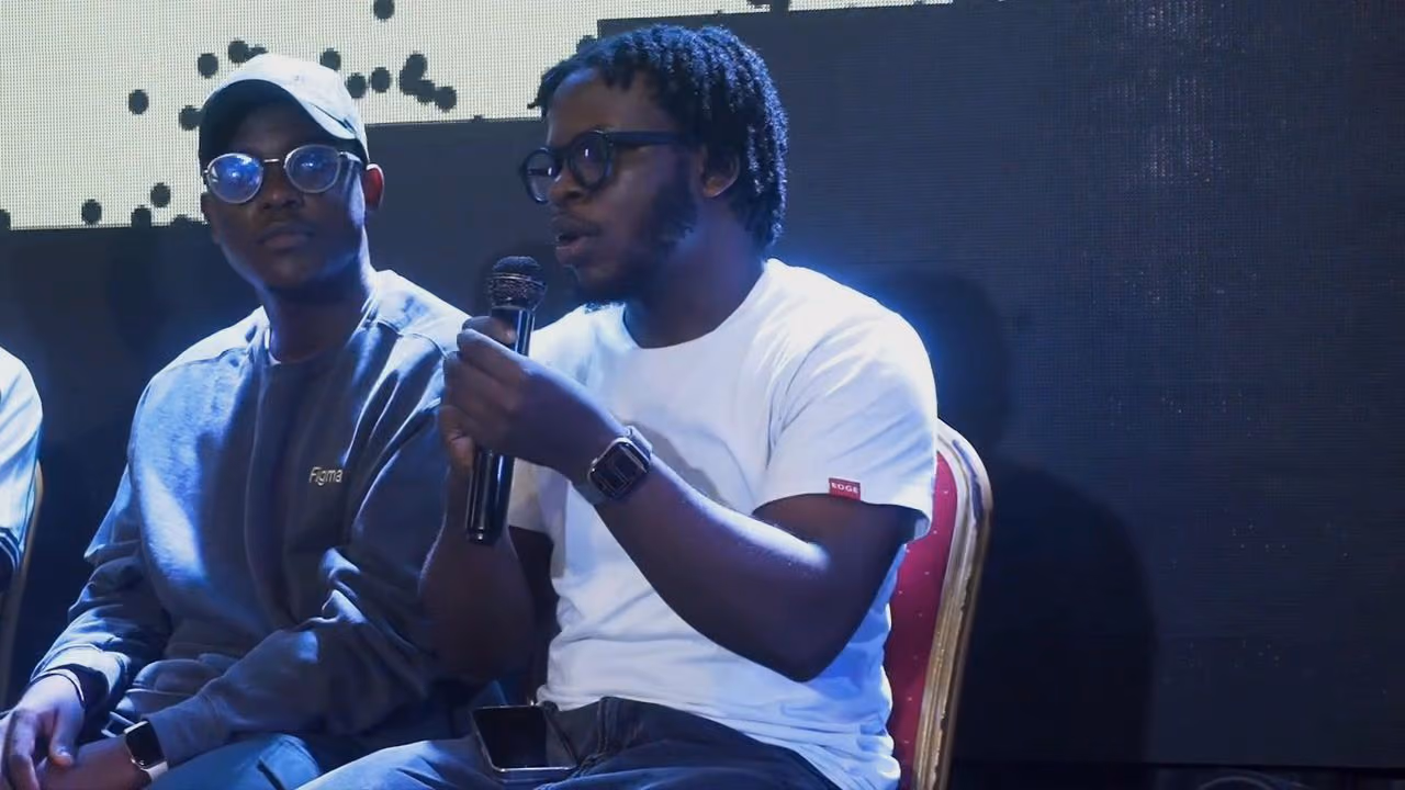 Close-up of two panellists, one in a white tee answering into a microphone