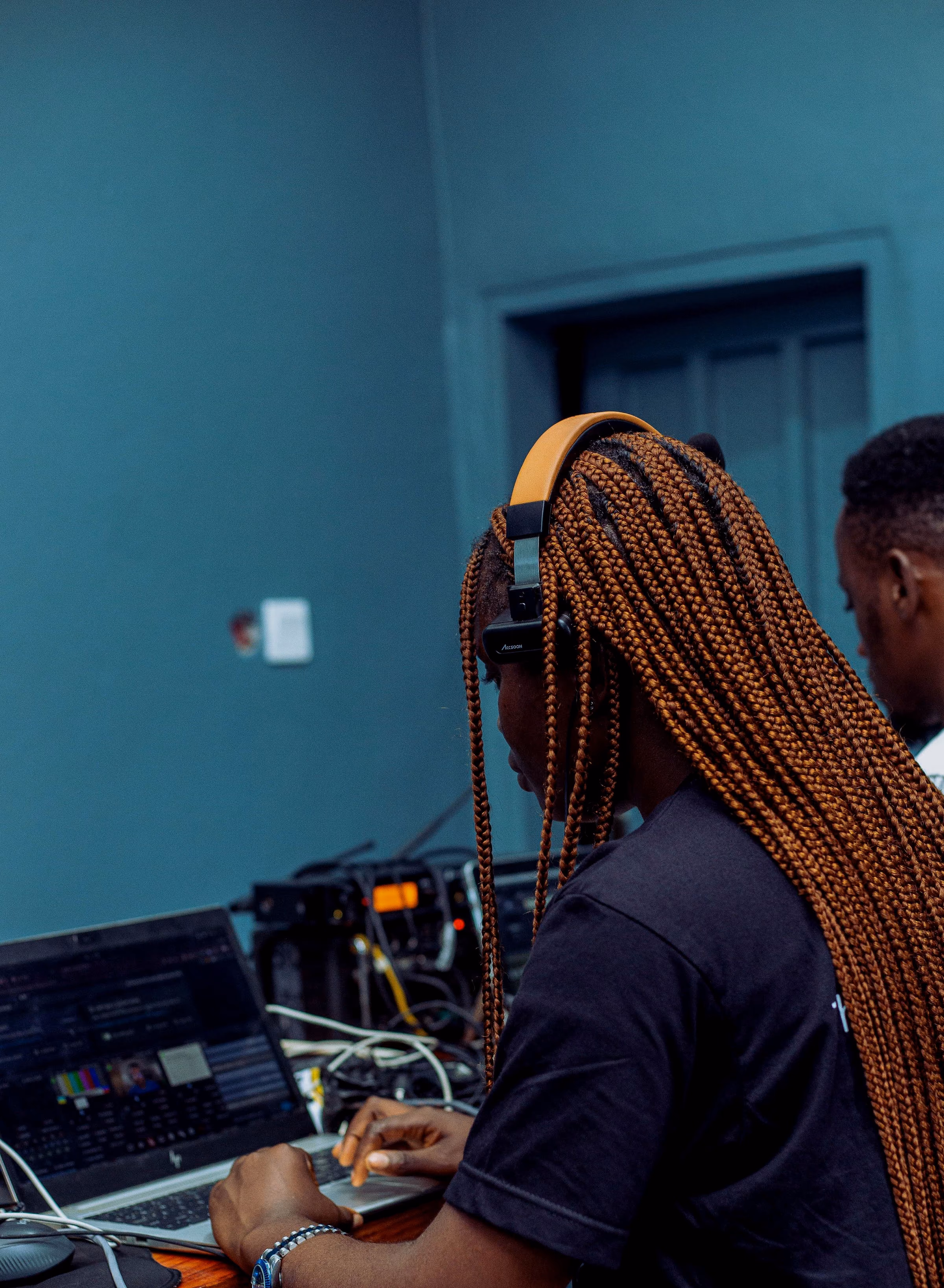 Crew member with long braids adjusting an audio mixer in the teal control room