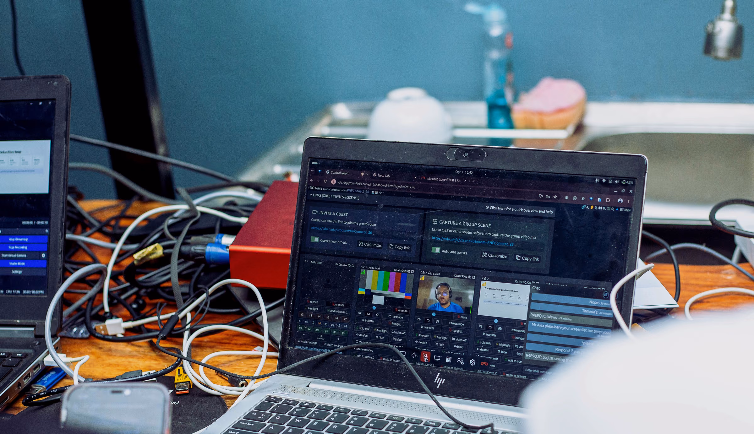 Laptop running switching software on a cluttered desk of cables and audio interfaces