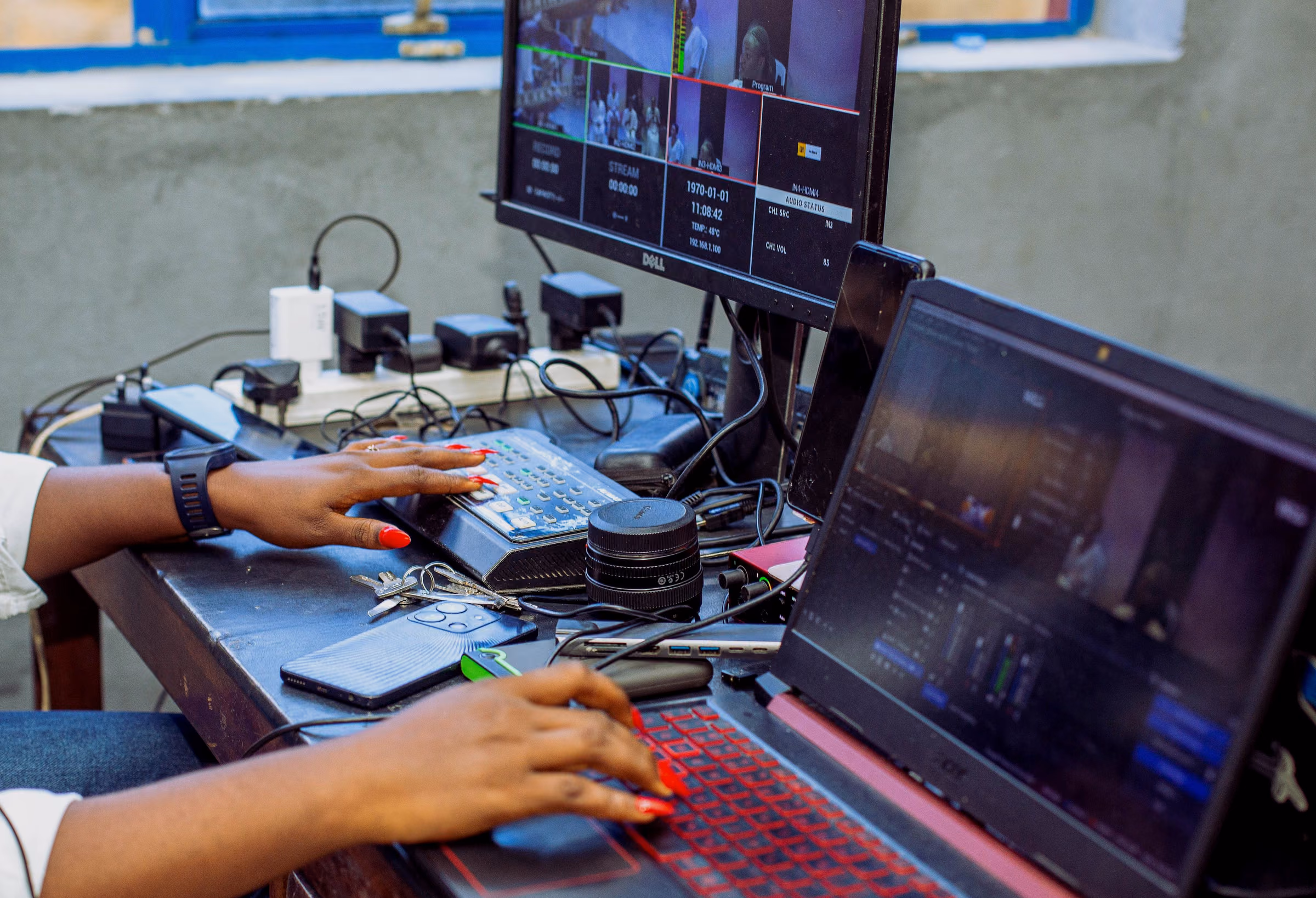 Hands on a switcher and laptop beside a monitor of camera feeds