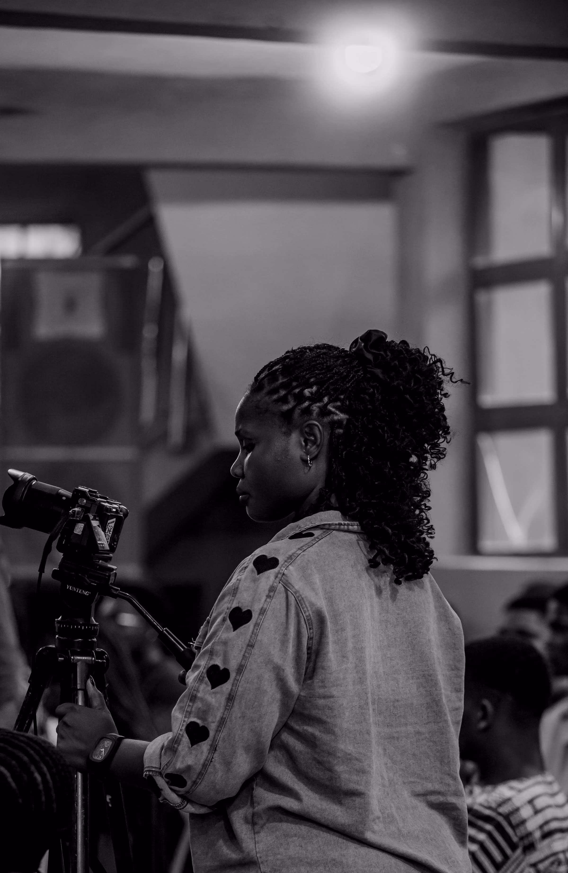 Black-and-white frame of a camera operator on a tripod among the congregation