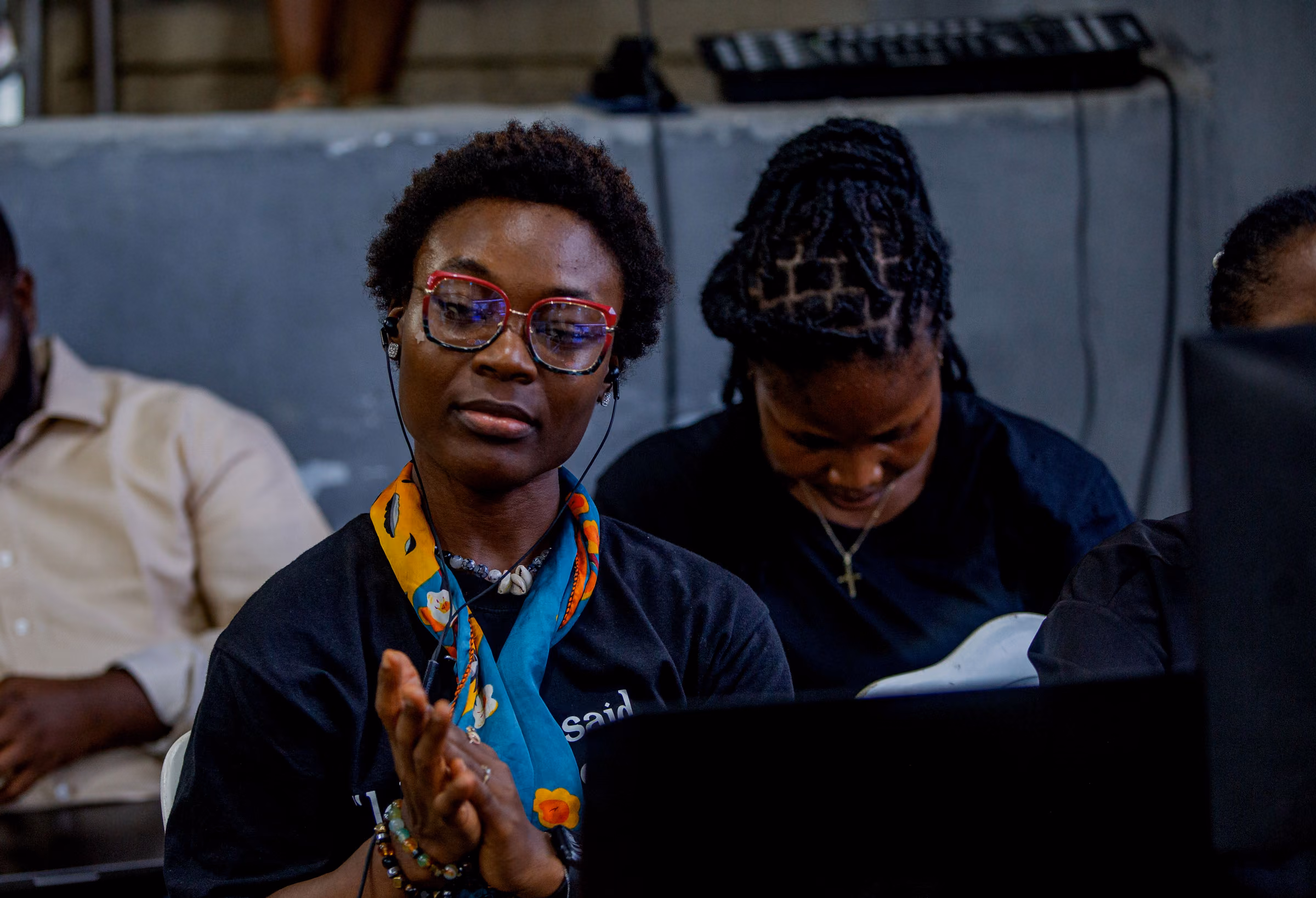 Crew member in an ankara scarf and headset clapping at a laptop during a service