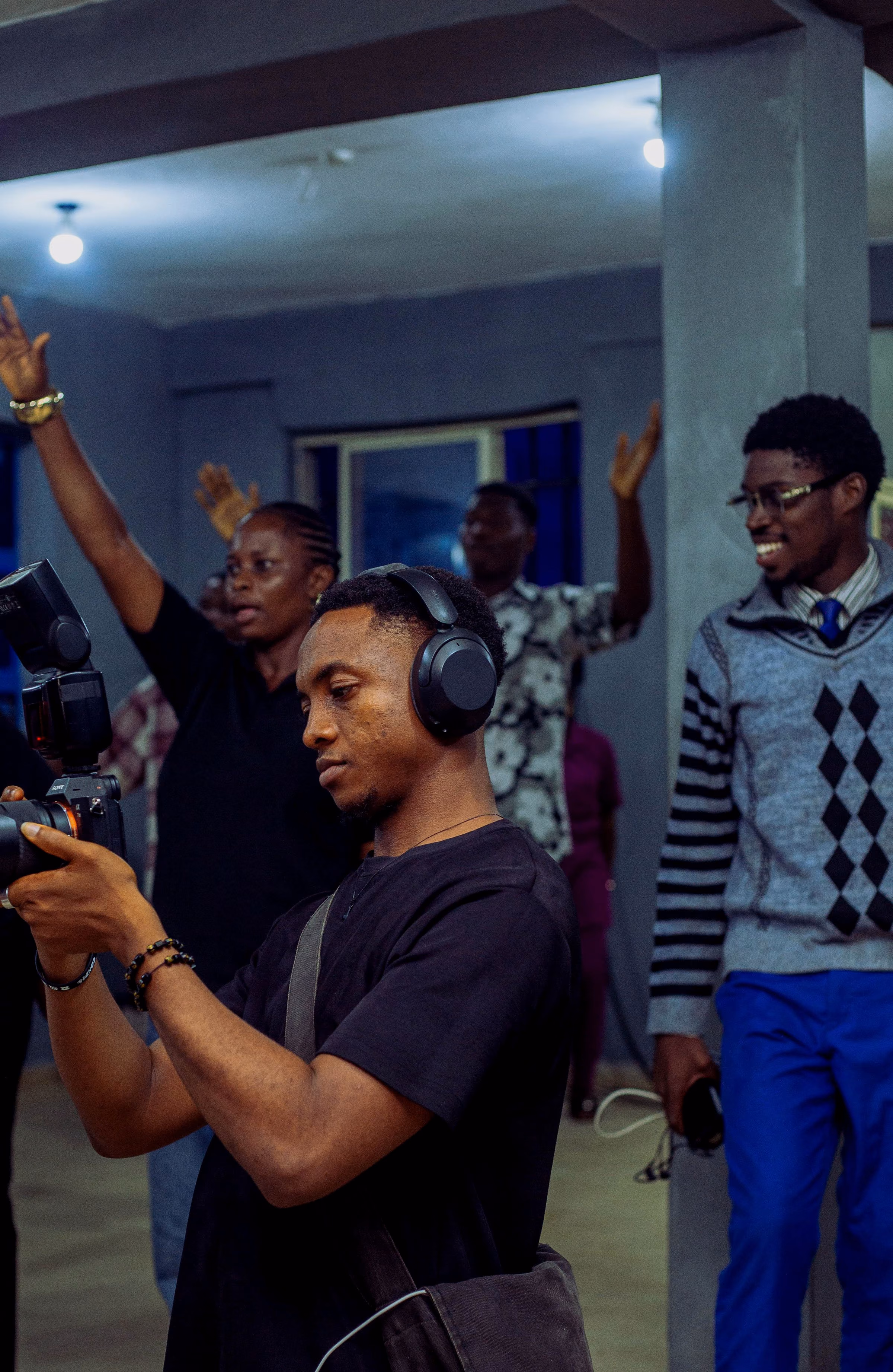 Operator in a headset lining up a camera while worshippers raise their hands behind