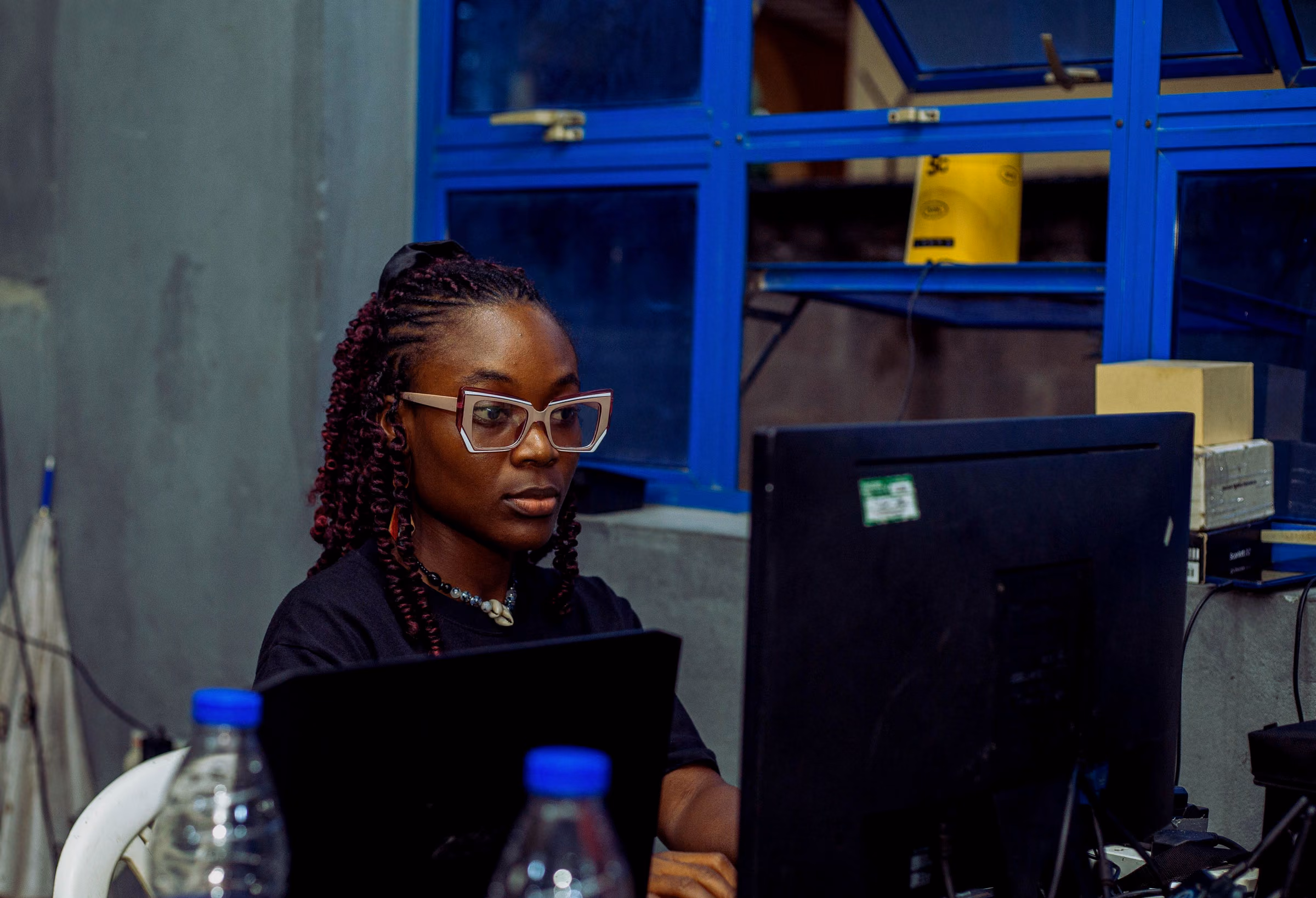 Crew member with glasses working at a laptop and monitor in a concrete room